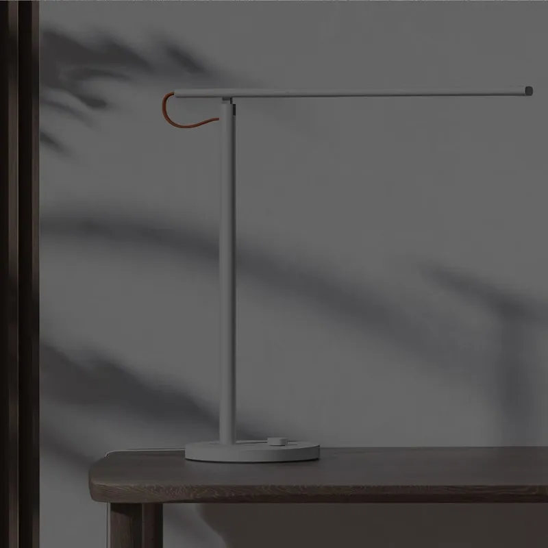 Xiaomi Mi LED Desk Lamp 1S đặt trên bàn gỗ sát tường, thanh đèn vươn ngang mặt bàn