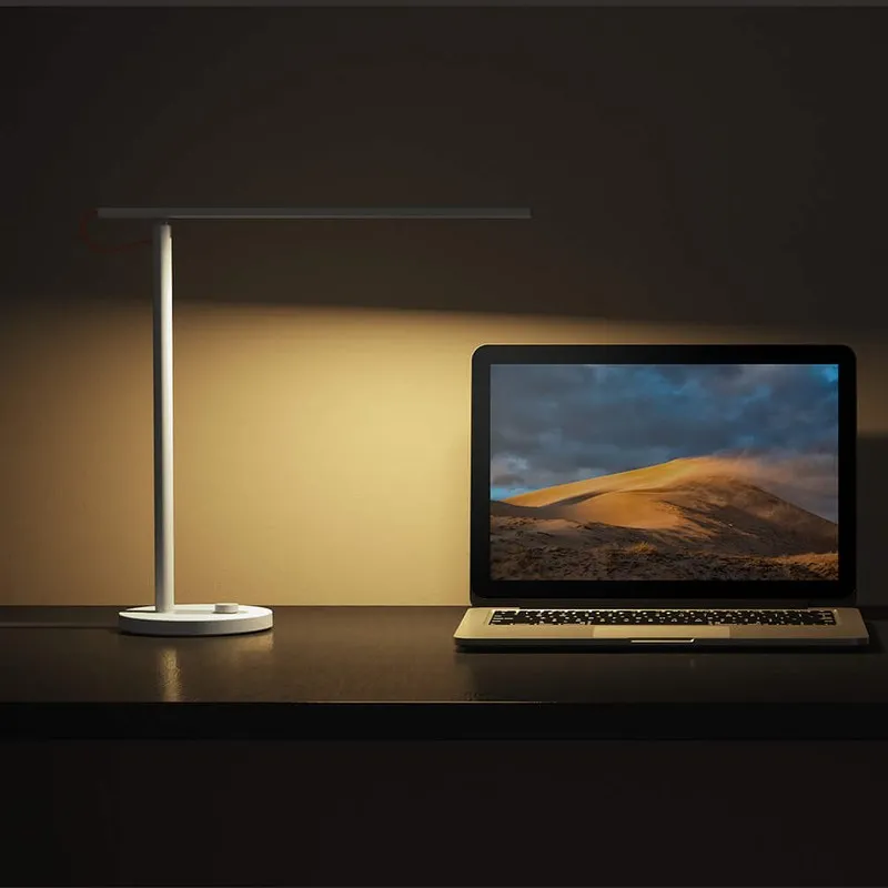 Xiaomi Mi LED Desk Lamp 1S bật ánh vàng ấm rọi xuống laptop trên bàn trong phòng tối