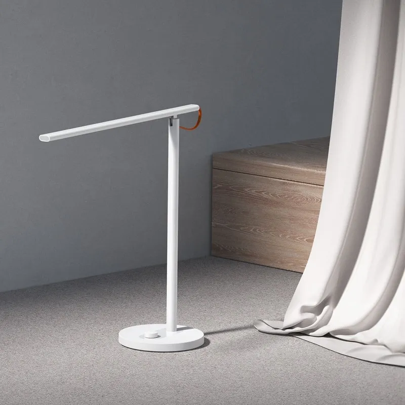 Xiaomi Mi LED Desk Lamp 1S đứng trên sàn thảm xám cạnh rèm trắng, thanh đèn chếch lên